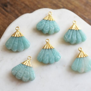 May include: Six teal green gemstone pendants with gold accents in the shape of a fan. The pendants are on a white surface.
