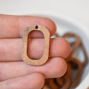 May include: A wooden oval pendant with a hole at the top. The pendant is light brown in color and has a smooth finish.