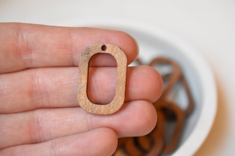 May include: A wooden oval pendant with a hole at the top. The pendant is light brown in color and has a smooth finish.