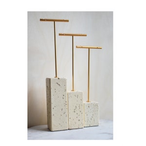 May include: Three gold earring stands on a set of three white concrete bases. The stands are different heights.