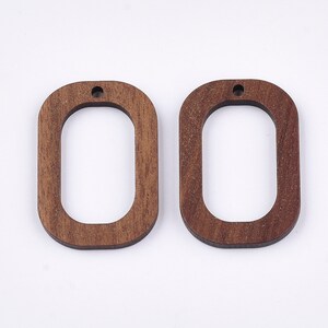 May include: Two unfinished wooden oval-shaped earring blanks with a hole at the top. The blanks are a light brown color.