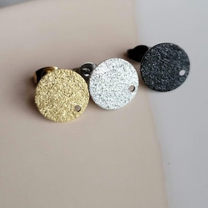 May include: Three round earrings with a textured surface. The earrings are gold, silver, and black.