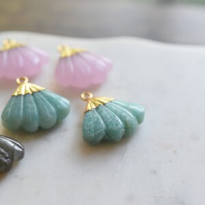 May include: Assortment of five shell-shaped pendants with gold accents. The pendants are made of various materials, including green, pink, and gray stones.