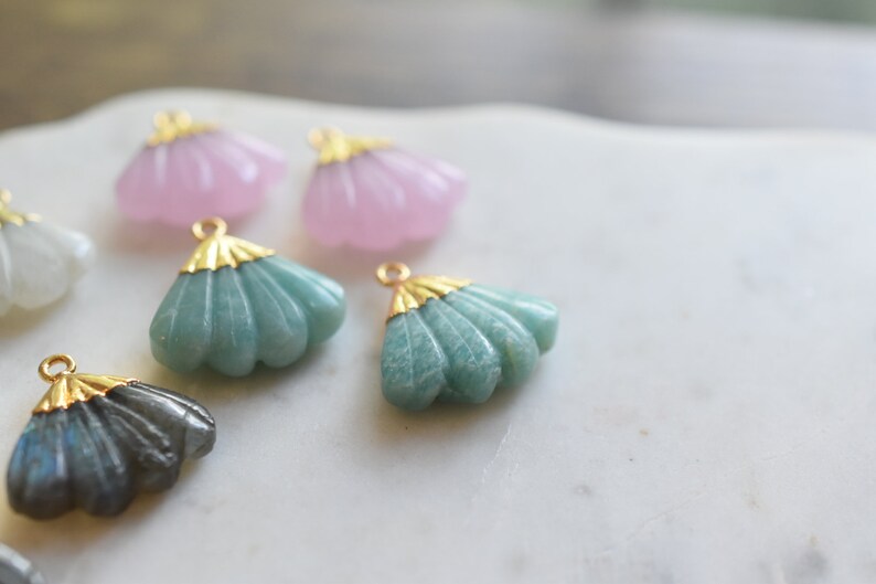 May include: Assortment of five shell-shaped pendants with gold accents. The pendants are made of various materials, including green, pink, and gray stones.