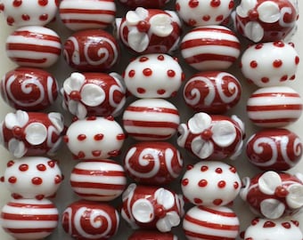 Puede incluir: Una colección de cuentas de vidrio dispuestas en filas verticales, con un esquema de color rojo y blanco. Las cuentas muestran varios patrones, incluyendo rayas horizontales, puntos rojos en relieve sobre superficies blancas, espirales y flores.