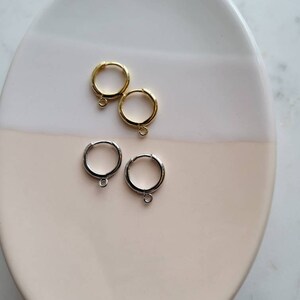 Puede incluir: Dos pares de pendientes de aro, un par es dorado y el otro par es plateado. Los pendientes est&aacute;n en un plato blanco y rosa.