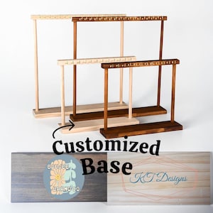 May include: Wooden jewelry display stands in various shades of brown and natural wood. Each stand has a horizontal bar with small pegs for hanging jewelry. The stands are on a white surface. The image also shows a customized base with the text "Customized Base".