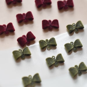 May include: A collection of burgundy and olive green velvet bows. The bows are arranged on a white and pink plate.