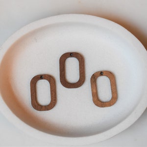 May include: Three unfinished wooden oval shapes with a hole in the top. The ovals are light brown and have a smooth surface.