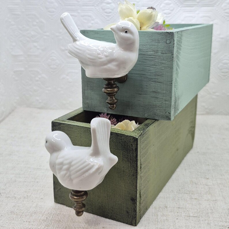 May include: Two wooden boxes with white porcelain bird drawer pulls. The top box is light blue and the bottom box is dark green.