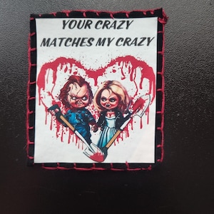 May include: A rectangular patch with a black border and red stitching. The patch features a graphic of two dolls with bloody shovels inside a red heart shape. The text "YOUR CRAZY MATCHES MY CRAZY" is above the dolls.
