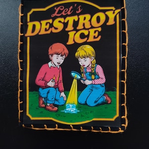May include: A rectangular patch with the text "Let's DESTROY ICE" in yellow and white. The image depicts two children kneeling on green grass, one holding a candle, the other a magnifying glass, focused on a block of ice. The patch has a black border with orange stitching.