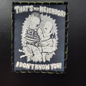 May include: A square patch with a black background and green stitching. The patch features a black and white illustration of an ICE police officer and a child with the text "THAT'S MY NEIGHBOR! I DON'T KNOW YOU!"
