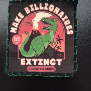 May include: A black patch with green stitching around the edges. The patch features a green dinosaur illustration with the words "MAKE BILLIONAIRES EXTINCT" and "A HOW-TO GUIDE" in white text. A volcano and palm trees are also visible.