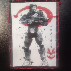Peut inclure: Écusson brodé représentant un soldat tenant une arme, avec un cercle rouge en arrière-plan. Le patch a une bordure noire avec des coutures rouges et du texte japonais.