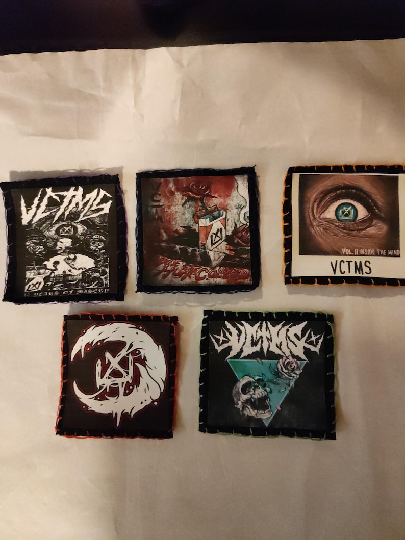 May include: Five square patches with black borders and stitched edges. The patches feature various designs, including a skull, eye, and band logos. The patches are in black, white, red, and blue.