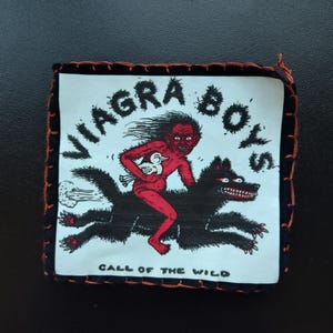 May include: Square patch with the text "VIAGRA BOYS" in white, featuring a red cartoon figure riding a black wolf. The phrase "CALL OF THE WILD" is below the illustration. The patch has a black border with orange stitching.