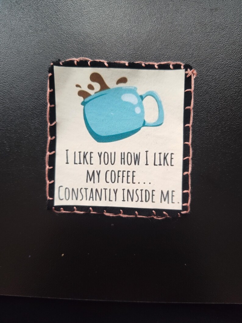 K&ouml;nnte beinhalten: Ein Stoffaufn&auml;her mit einem hellblauen Kaffeetassen-Design und dem Text "I LIKE YOU HOW I LIKE MY COFFEE... CONSTANTLY INSIDE ME." Der Aufn&auml;her hat einen schwarzen Rand mit rosa N&auml;hten.