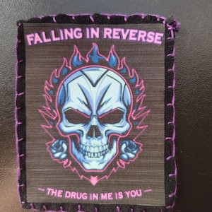May include: A square patch with the text "FALLING IN REVERSE" in pink above a blue and white skull design with pink flames. The text "THE DRUG IN ME IS YOU" is below the skull. The patch is bordered with black fabric and purple stitching.
