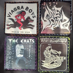 May include: Four square patches with stitched edges. The patches feature band logos and illustrations, including "VIAGRA BOYS" with a figure riding a wolf, "THE <HATS" with a beer can, and "TEEN MORTGAGE".
