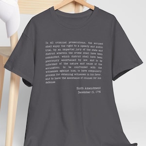 Könnte beinhalten: Dunkelgraues T-Shirt mit dem Text des sechsten Zusatzartikels zur US-Verfassung, einschließlich des Datums 15. Dezember 1791, in Weiß. Ein lässiges Kleidungsstück.