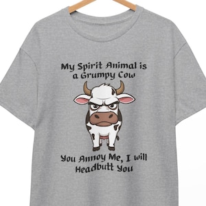 May include: A grey t-shirt with a grumpy cow graphic and the text "My Spirit Animal is a Grumpy Cow" and "You Annoy Me, I will Headbutt You". The cow is black and white with brown accents and a stern expression.