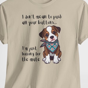 May include: Beige t-shirt with a graphic of a brown and white puppy wearing a blue bandana. The text on the shirt reads, "I don't mean to push all your buttons... I'm just looking for the mute."