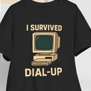 May include: Black t-shirt with the text "I SURVIVED" above a retro computer graphic and the words "DIAL-UP" below. The computer is beige with a green screen. A fun, nostalgic design.