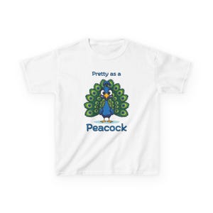 Op de afbeelding: Wit kinder-T-shirt met een cartoon pauw met een blauw lichaam, groene en blauwe staartveren en de tekst "Pretty as a Peacock" in het blauw. Het T-shirt is voor kinderen.