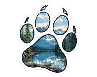 Puede incluir: Una pegatina blanca con forma de huella de oso. Cada almohadilla de la pata presenta una escena de paisaje diferente: un lago con montañas, un bosque y un cielo nublado. El diseño general es una ilustración con temática de la naturaleza.