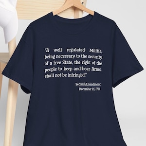 Può includere: T-shirt blu navy con testo bianco. Il testo recita: «Una milizia ben regolamentata...non sarà violata». Sotto il testo c'è «Secondo emendamento, 15 dicembre 1791».