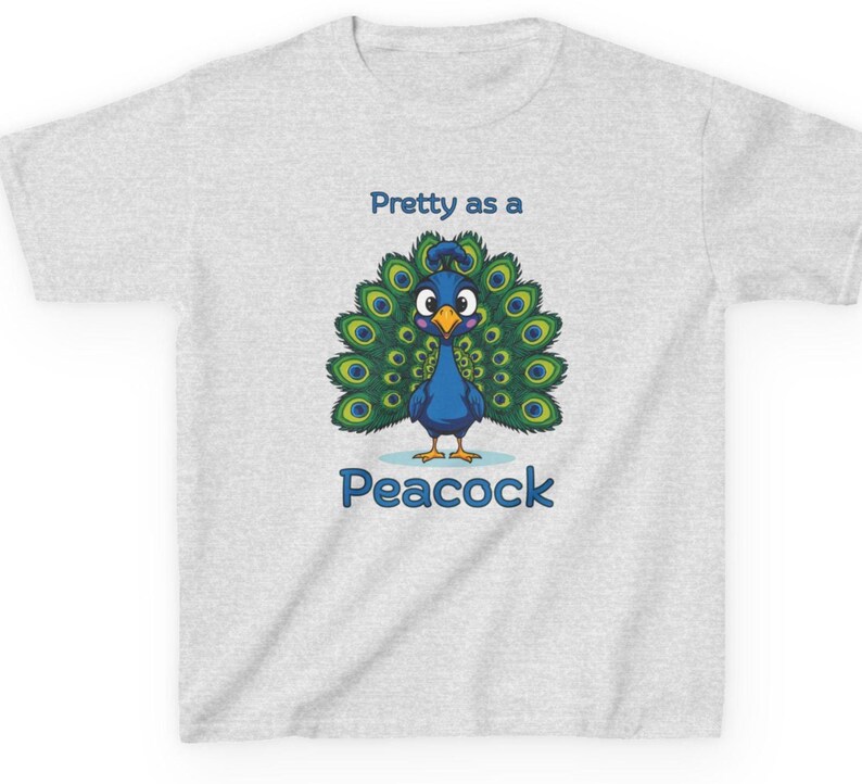 Op de afbeelding: Lichtgrijs t-shirt met een cartoon pauw ontwerp. De pauw is blauw met groene en gele staartveren. De tekst "Pretty as a Peacock" en "Peacock" zijn blauw.