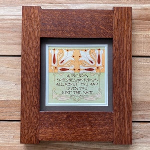 May include: A framed art print with a quote about friendship. The print features a decorative design with white and red floral elements. The frame is made of dark brown wood.