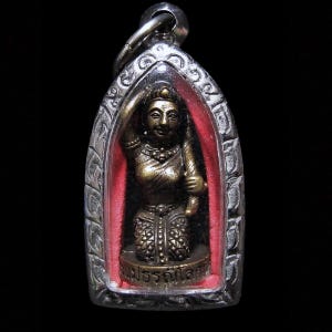 Op de afbeelding: Een kleine, sierlijke hanger met een bronzen figuur die een staf vasthoudt, tegen een rode achtergrond. De figuur bevindt zich in een zilverkleurig, boogvormig frame met ingewikkelde details. De hanger heeft een lus om op te hangen.