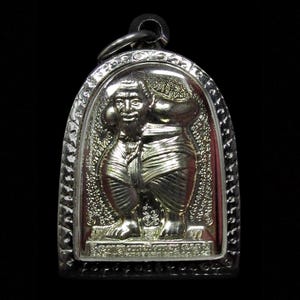 Può includere: Un ciondolo d'argento raffigurante un rilievo dettagliato di una figura con barba e abiti tradizionali. Il ciondolo ha una parte superiore ad arco e un bordo strutturato. La figura è in piedi e sembra tenere qualcosa. Lo sfondo è scuro.