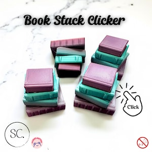 May include: A collection of 3D-printed book stack clickers in shades of purple, teal, and brown. The text "Book Stack Clicker" is displayed at the top. A hand icon with the word "Click" is also present. The product is labeled as suitable for ages 0-3.
