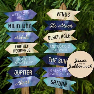 Puede incluir: Un conjunto de 12 señales de flecha con temática espacial con fondos inspirados en la galaxia. Las señales presentan nombres de cuerpos celestes y términos relacionados con el espacio, como "Cinturón de asteroides", "Vía Láctea", "Venus", "La Luna", "Agujero negro", "Lluvia de meteoritos", "El Sol", "Puerto espacial galáctico", "Saturno", "Nebulosa", "Residencia terrenal", "Nave espacial cohete", "Júpiter" y "Extraterrestres".
