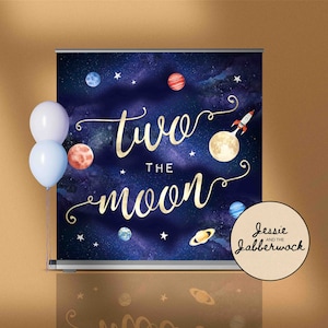 May include: A blue and black space-themed backdrop with gold lettering that reads "two the moon". The backdrop features planets, stars, and a rocket ship. The text "Jessie and the Jabberwock" is in a circle at the bottom right corner.