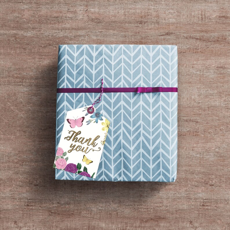 May include: A blue and white gift box with a chevron pattern. A white gift tag with a floral design and butterflies is attached to the box with a purple ribbon. The tag says "Thank you" in gold lettering.