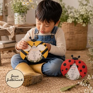 May include: Two circular party invitations shaped like insects. One invitation features yellow and black bee wings, while the other displays red and black ladybug wings. Both cards include printed text details for a birthday celebration.