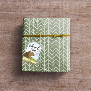 Peut inclure: Une bo&icirc;te cadeau verte &agrave; motif chevron, emball&eacute;e d'un ruban dor&eacute;. Une &eacute;tiquette cadeau avec une illustration d'un ours brun et le texte "Merci" et "Presque beaucoup !" est attach&eacute;e &agrave; la bo&icirc;te.