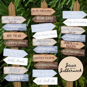 May include: A collection of wooden arrow signs, each pointing in a different direction and displaying phrases such as "Bear Ears" and "Cub Ball Pit". The signs have a weathered appearance with a mix of fonts and colours, some with a blue gingham pattern.