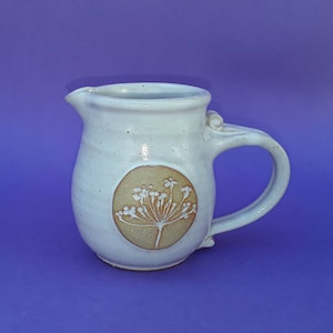 May include: A white ceramic jug with a brown and white floral design. The jug has a rounded body and a handle.