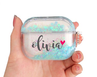 May include: A clear plastic case with a blue and white glitter design. The case has a small pink heart and the name "Olivia" written on it.