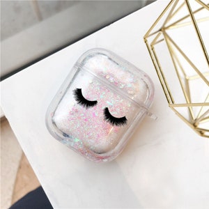 May include: Clear plastic case for AirPods with a glittery pink and white design. The case has a black eyelash design on the front.