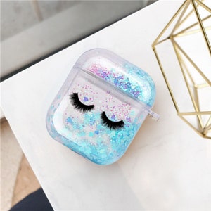 May include: Clear plastic case for AirPods with a blue and pink glitter design and black eyelashes printed on the front.