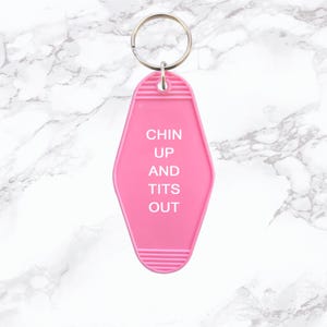May include: Pink motel key chain with the text "Chin Up And Tits Out" in white lettering.