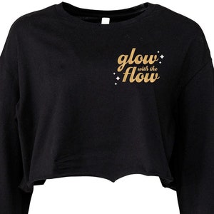 May include: Black long-sleeved cropped sweatshirt with a gold graphic that says "glow with the flow".