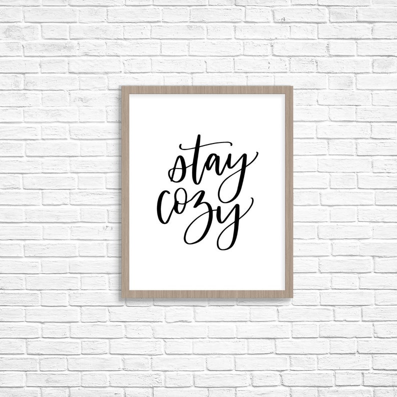 May include: A framed print with the text "stay cozy" written in black cursive script on a white background.