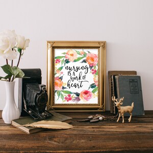 May include: A gold framed print with a watercolor floral wreath and the text "nursing is a work of heart".